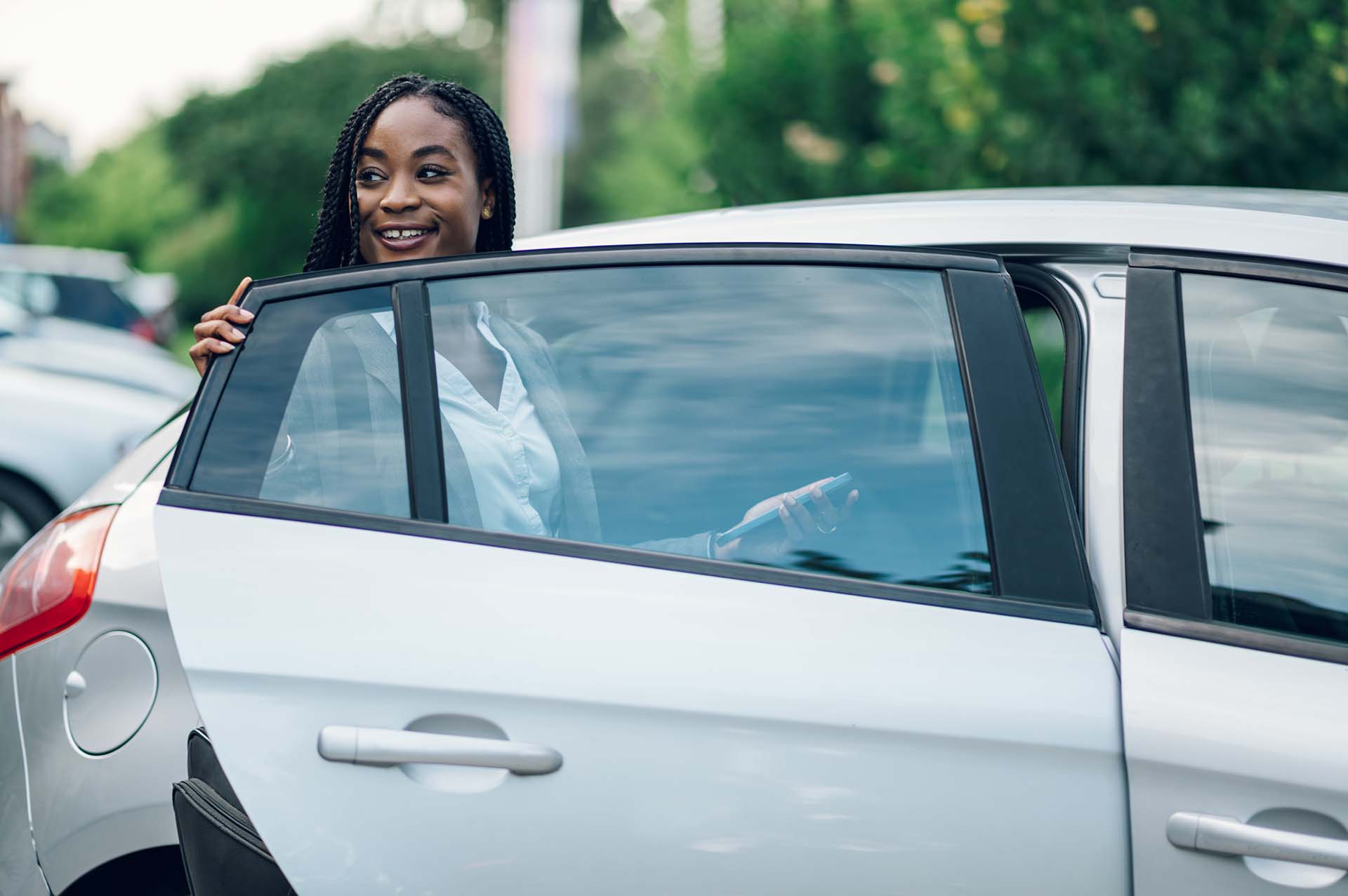 Portrait of successful african american business woman holding car door while getting inside. Attractive CEO black female executive wearing a suit and braids. Copy space. Successful woman in business.