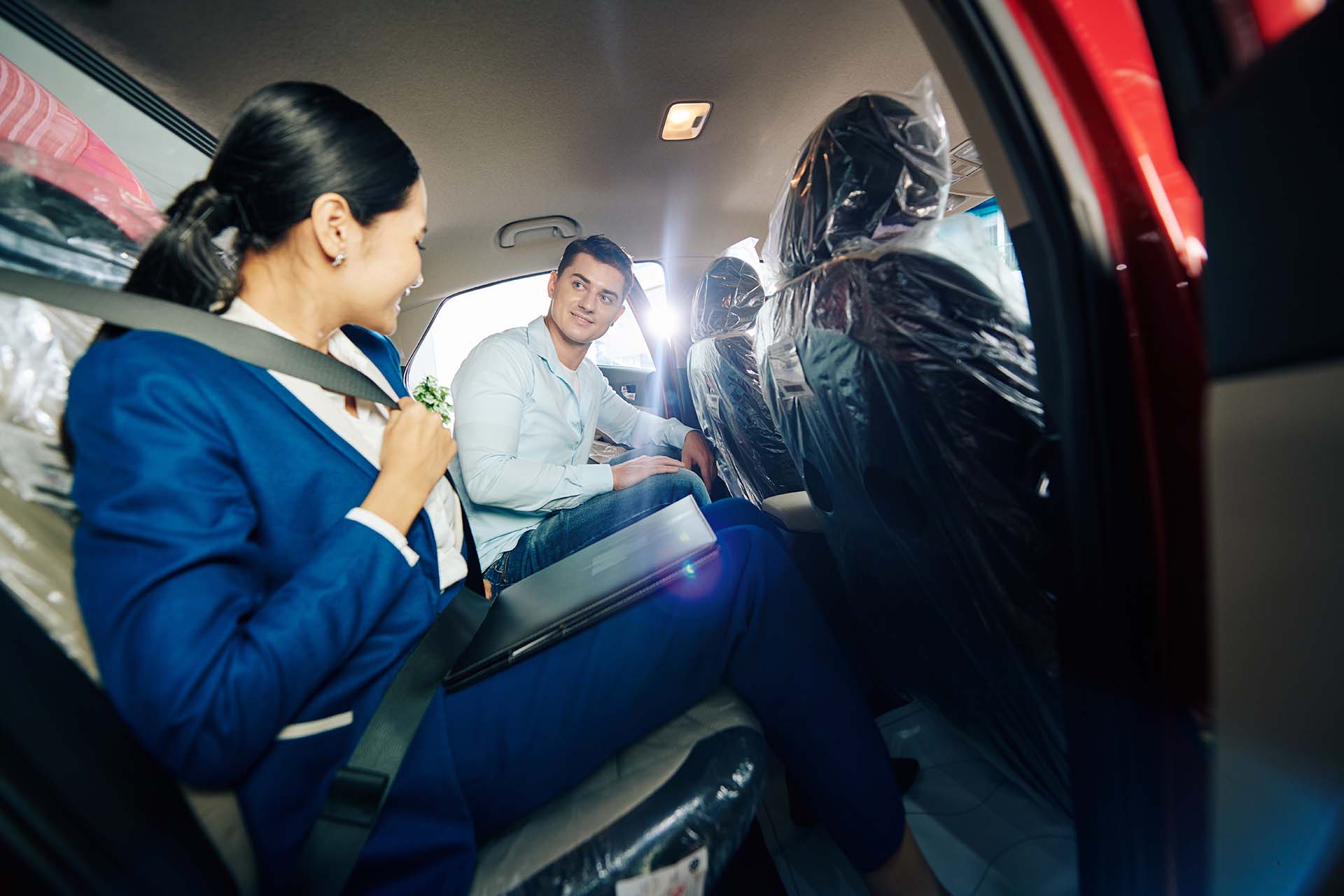 Female car dealership manager showing customer how to fasten seat belts on backseat