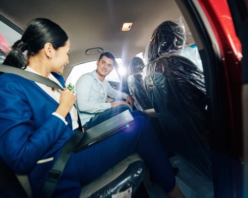 Female car dealership manager showing customer how to fasten seat belts on backseat